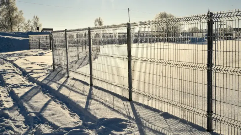 Lumega kaetud jalgpalliväljak ja piirdeaed päikeselisel talvepäeval Eestis.