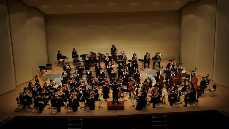 Orkester esinemas kontserdilaval koos dirigendiga pidulikus ja suurejoonelises atmosfääris.