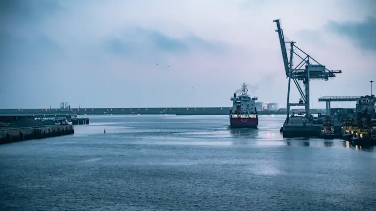 Kaubalaev ja sadamakraanad mere ääres, mis sümboliseerivad rahvusvahelist kaubandust ja logistikat.