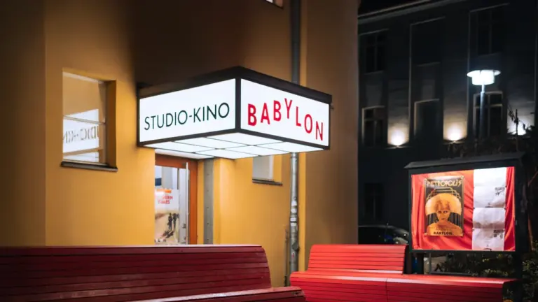 Babüloni kino sissepääs õhtusel ajal koos valgustatud sildi ja punaste pinkidega.