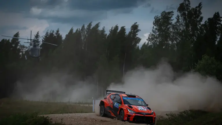 Ralliauto sõitmas tolmulisel kruusateel Eestimaa looduses, taustal on helikopter ja metsatukk.