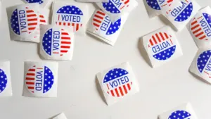 Valged ümmargused kleebised tekstiga I VOTED, kaunistatud USA lipu tähtede ja triipudega heledal taustal.