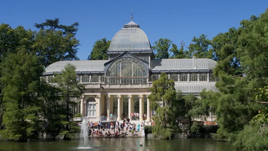 Crystal Palace klaasist hoone peegeldumas järveveel päikeselisel suvepäeval, ümbritsetud roheliste puudega.