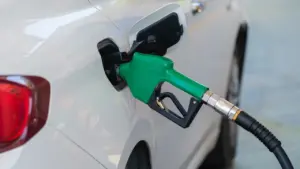 Valge auto tankimine bensiinijaamas, fookus kütusepüstolil ja kütusepaagi luugil.